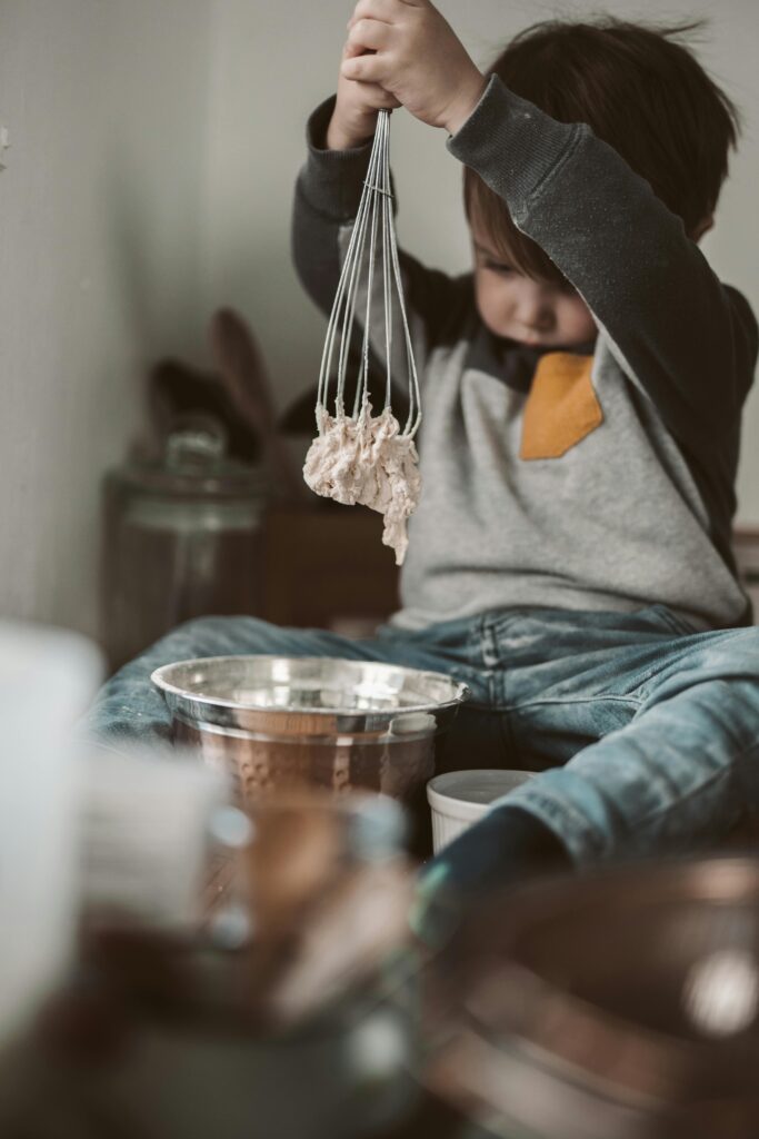 Child playing with dough using whisk, showcasing curiosity and creativity indoors.