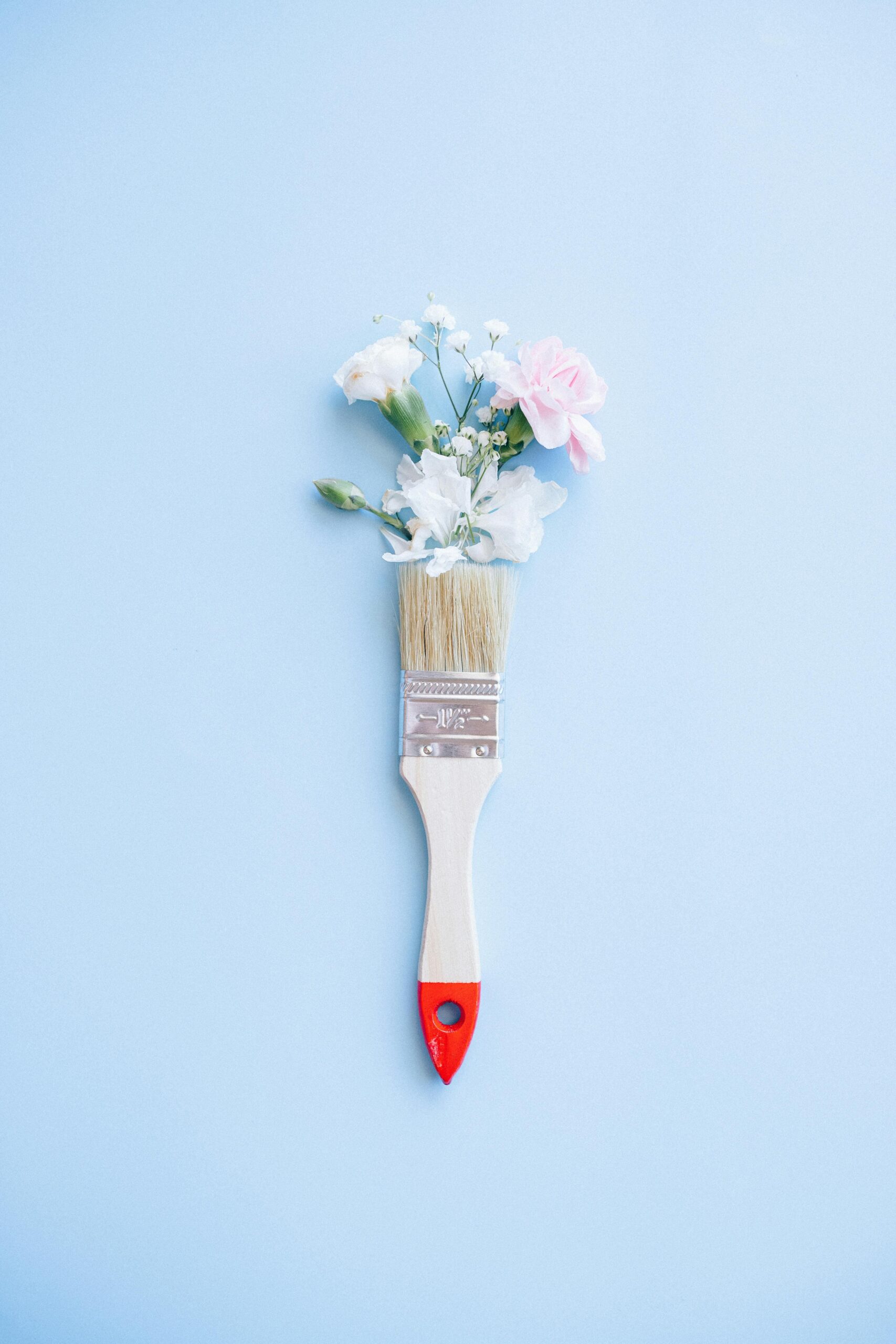 A minimalist image of a paintbrush adorned with delicate flowers against a blue background.