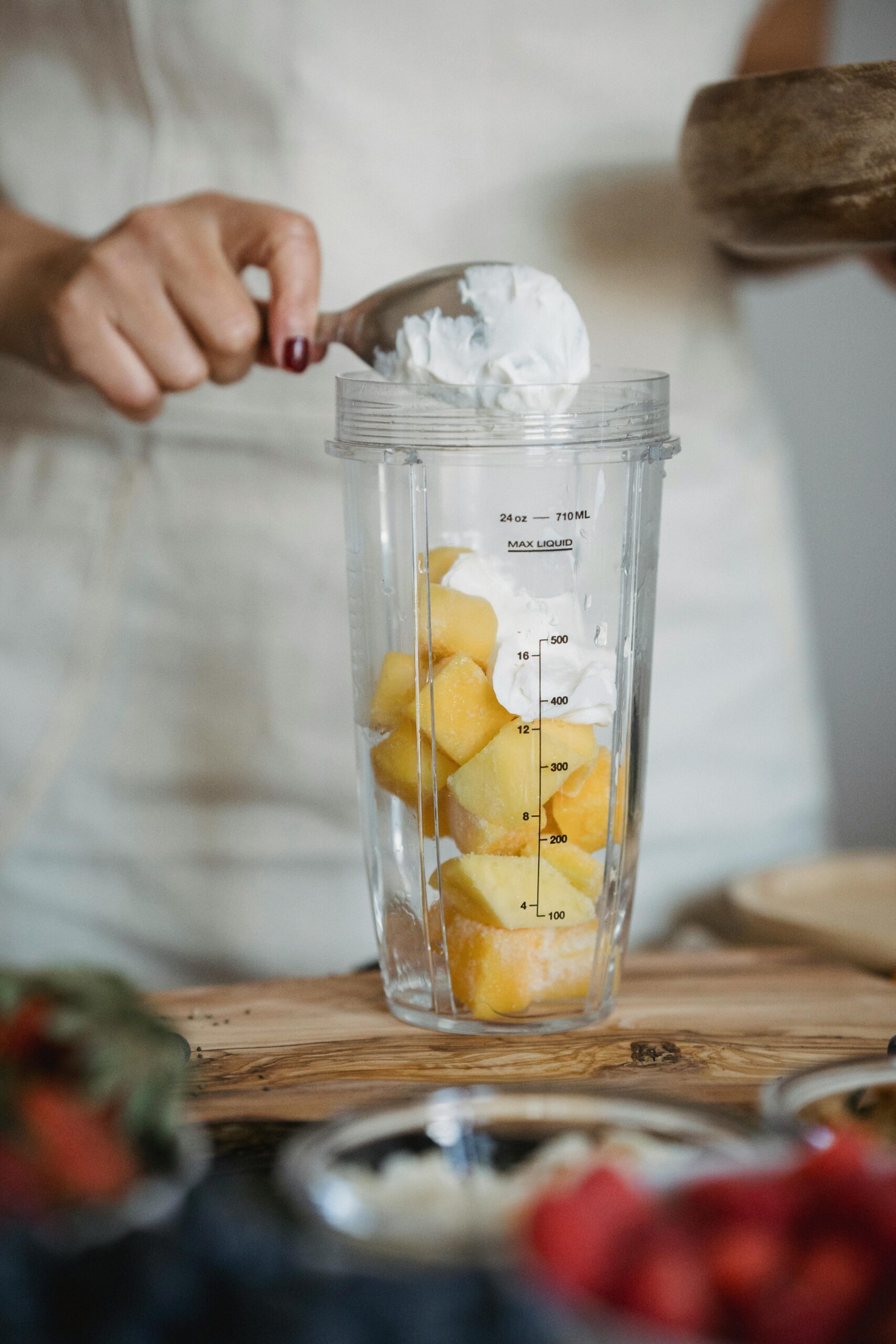 A person making a pineapple smoothie with whipped cream in a blender jar indoors.